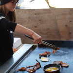 Girl cooking bacon and eggs on a grill